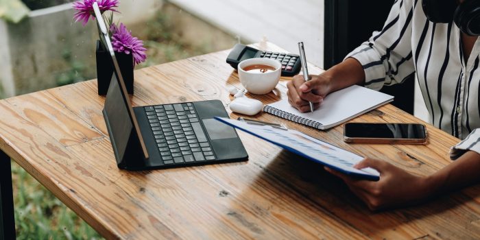 shot of female accounting bookeeper providing accounting service for small businesses, sitting at desk with portable computer, holding pen to make notes and using calculator, woman using digital tablet and calculator.